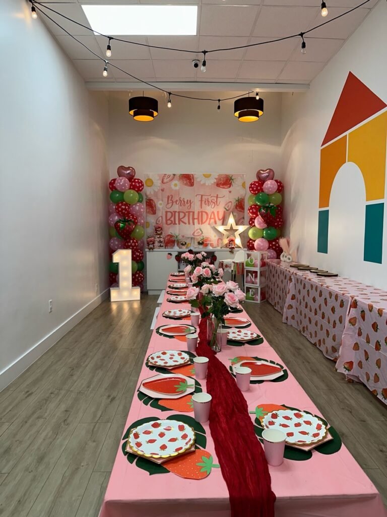 Berry First Birthday party theme with strawberry decorations, red balloon garland, and fruit-themed desserts at Kids Hideout Fort Lauderdale