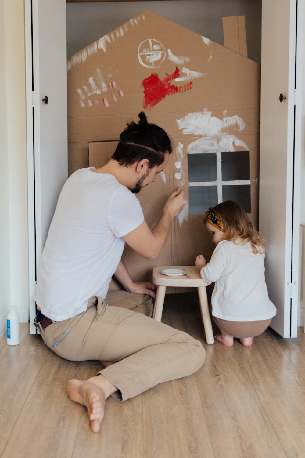 Father and daughter painting a cardboard house together in a creative activity class
