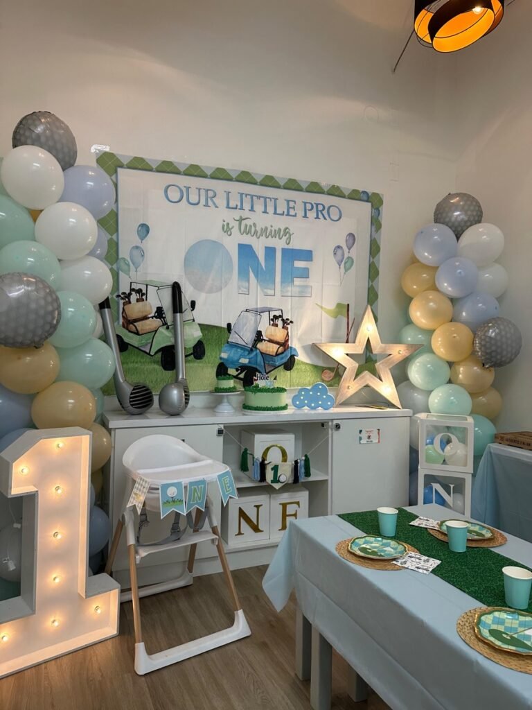 Hole in ONE golf first birthday party theme with golf cart decorations and green balloon garland at Kids Hideout Fort Lauderdale