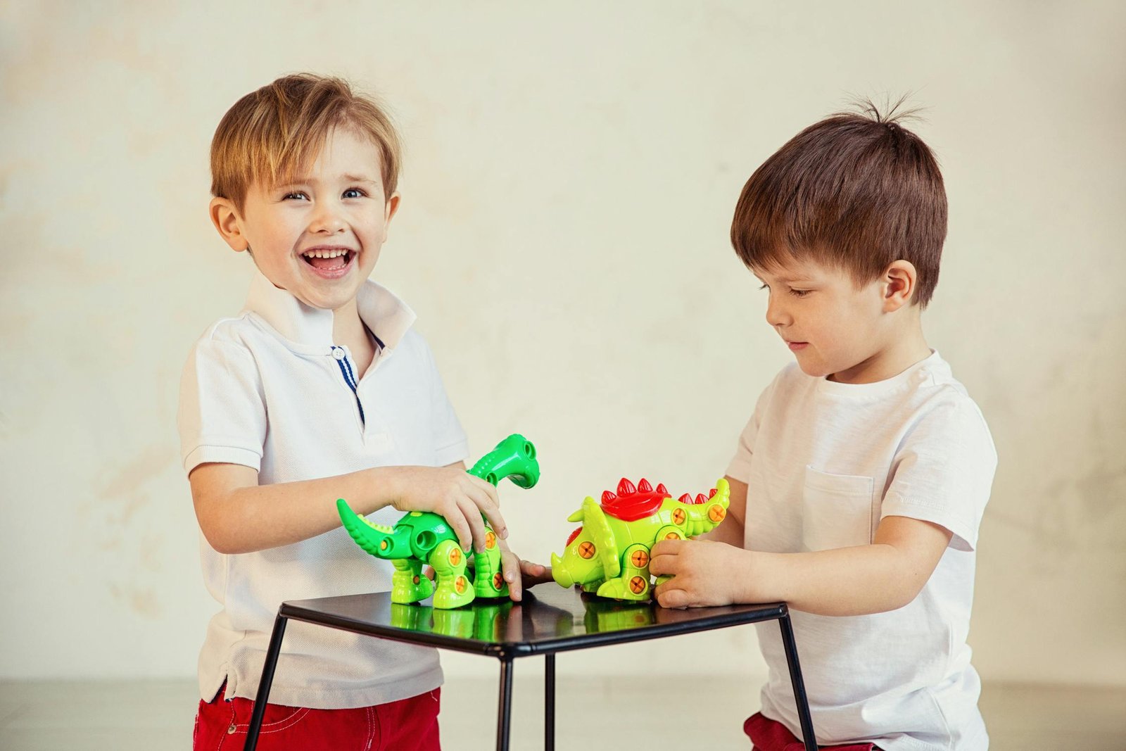 Two boys laughing and playing with toy dinosaurs together at an indoor play space