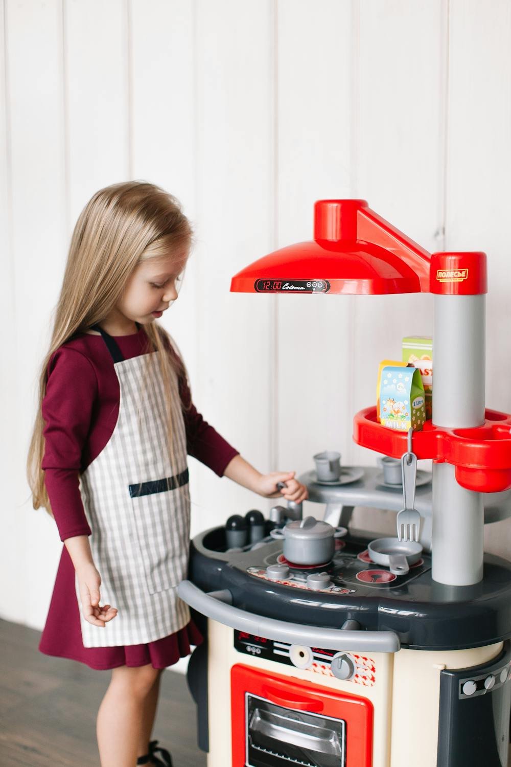 Girl wearing an apron playing on a miniature toy kitchen pretending to cook