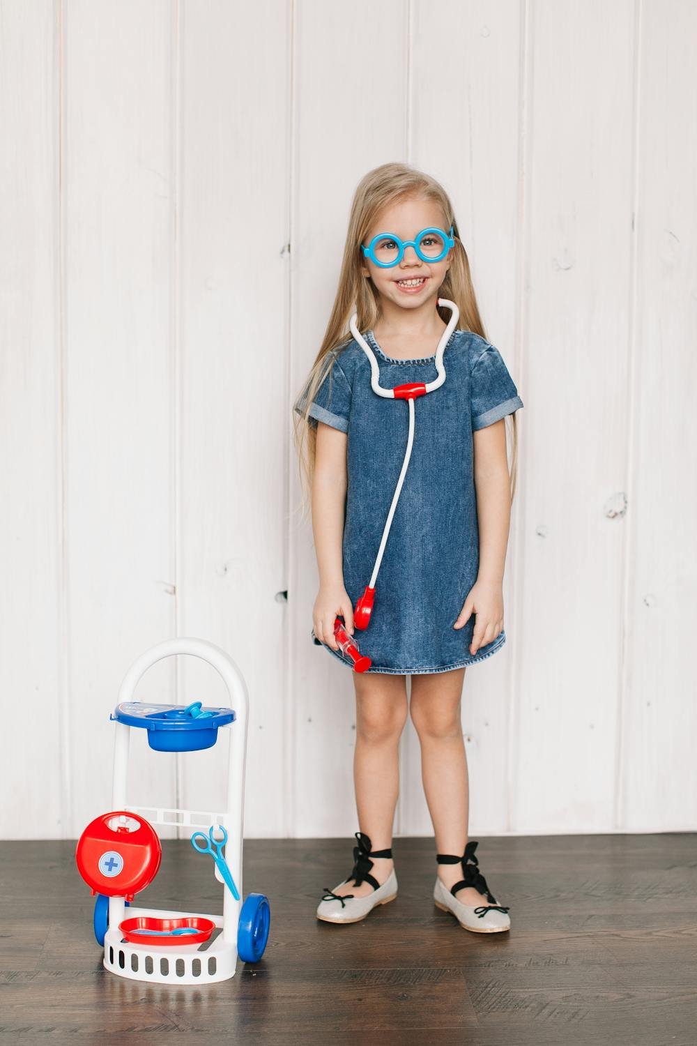 Girl in a blue dress holding a toy stethoscope pretending to be a doctor